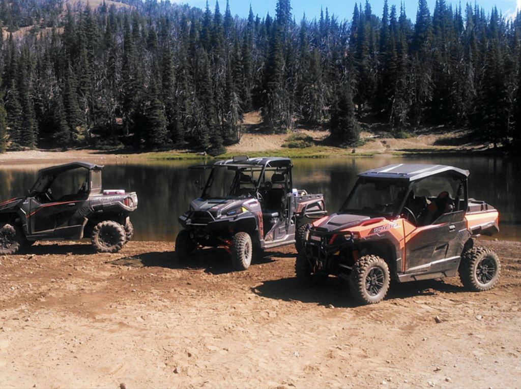 side by sides and ATV next to a lake on a trail